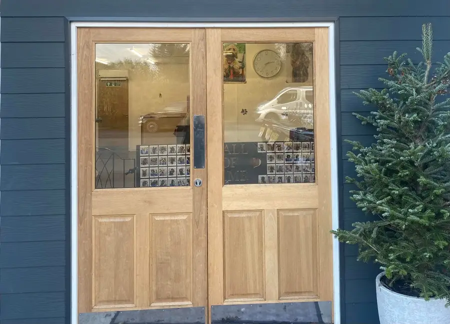 The salon entrance: oak double doors with glass panels set in dark grey cladding, a wall of dog photos in the window, and a small fir tree in a pot beside the door.